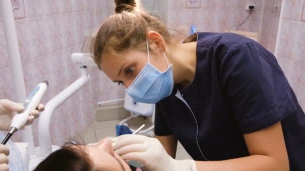Jovem dentista trata os dentes para um paciente e conversa com um assistente. Na recepção no doutor do stomatologist — Vídeo de Stock