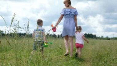 Genç Anne iki genç çocuklu alanında yaz aylarında çim üzerinde yürüme. Bir yolda mutlu aile.
