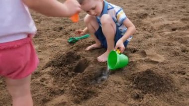 Küçük çocuk su bir kova kum bir deliğe dökülüyor. Plajda oynayan çocuklar