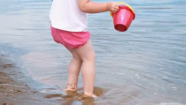 小女孩捡起水从水桶里倒进沙子特写 在沙滩上玩耍的孩子 — 图库视频影像