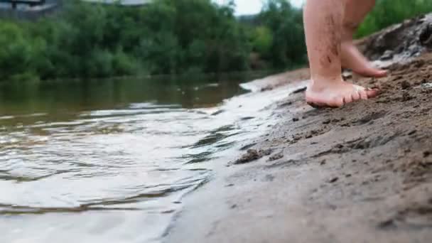 Vuile voeten van de baby. Kind wordt afgespeeld op de rivier met zand en een emmer — Stockvideo