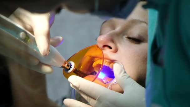 助手は、患者の歯のクローズ アップの歯科重合紫外線ランプに輝きます。歯科医への訪問します。 — ストック動画