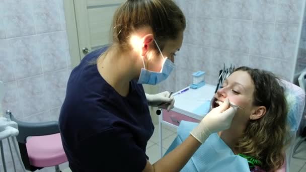 Bezoek aan de tandarts. Een orthodontist arts stelt ijzeren beugels voor een vrouw met een tandheelkundige fixatiemiddel in haar mond — Stockvideo