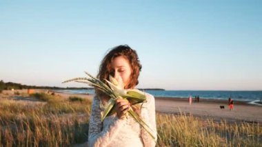 Bir gelinlik genç Avrupa kız deniz kenarında bir gelin el yapımı bir buket yaz aylarında gün batımında dolanıyor. Çim ve Mısır bir olağandışı düğün buket