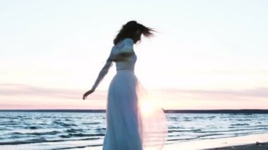 Gün batımında denizde el yapımı iplik özgün bir buket ile güzel Avrupa gelin. Sahilde dans bir gelinlik mutlu kadın