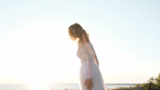 Європейська нареченої жінка в весільну сукню стрибає на заході сонця на пляжі біля моря влітку. — стокове відео