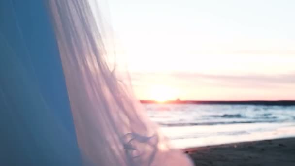 Panno trasparente svolazza nel vento al tramonto. Abito da sposa su uno sfondo di un paesaggio di mare nell'estate — Video Stock