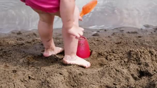 A menina está batendo um remo no balde, câmera lenta. Criança brinca com a natureza na areia na praia — Vídeo de Stock