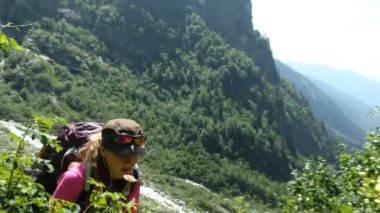 Genç kadın turist bir sırt çantası içinde kulaklık ile güzel bir manzara arka planda yokuş yukarı yükselir. Kız yaz aylarında yürüyerek tırmanıyor.