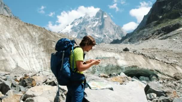 Guia turístico um homem com uma mochila estudando a rota no mapa e telefone GPS na caminhada na montanha — Vídeo de Stock