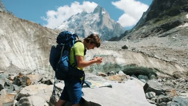 Турист с рюкзаком исследует маршрут на карте и телефоне GPS, добавляет карту и идет по маршруту в горном походе — стоковое видео