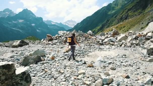 Touristische Wanderin wandert auf einer Wanderung in den Bergen durch ein steiniges Tal. Mädchen mit Rucksack auf der Abfahrt, Kamerafahrt — Stockvideo