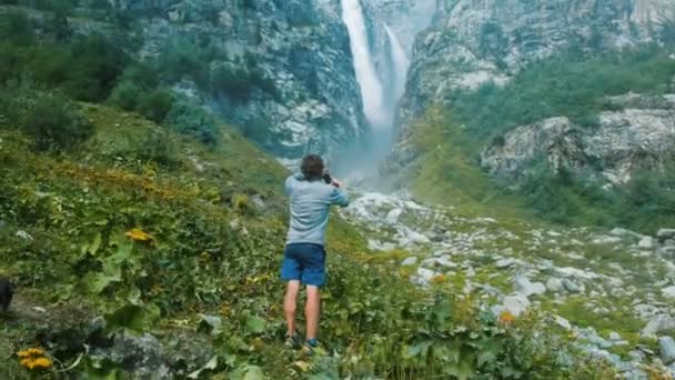 Toeristische man neemt een foto op een smartphone waterval in de bergen. Technologie in het wild. — Stockvideo