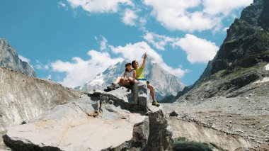 Aile evli çift turist bir kayaya oturan ve mountain view zevk. Adam bir kadın bir zam hugs ve dağ manzarası gösterir