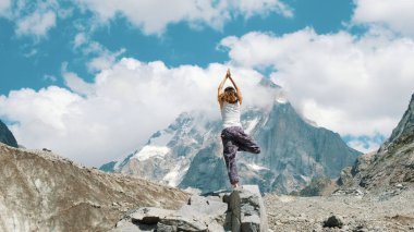 Kadın bir temel asana ağacı - vriksasana Yoga arka plan karlı dağda yürüyüşe üzerinde gerçekleştirir. Kızın jimnastik temiz havada yürüyüşe doğa üzerinde yaptığı