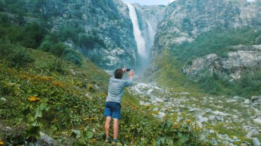 Turist adam bir smartphone şelale dağlarda bir resim alır. Vahşi teknoloji.
