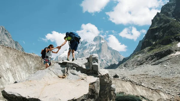 Un par de turistas con mochilas en la caminata suben a la cima de la piedra y se besan . — Foto de Stock