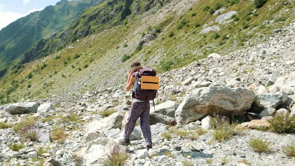 Turista mujer camina en un valle pedregoso en una caminata por las montañas. Chica con una mochila en el descenso, movimiento de la cámara — Foto de Stock