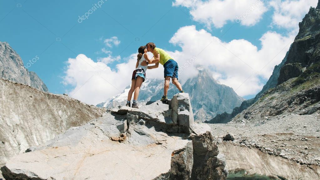 Family couple of tourists in the mountain trek climb to the top of the stone and raise their hands up, kiss and enjoy the climb. The concept of love, success and goal achievement