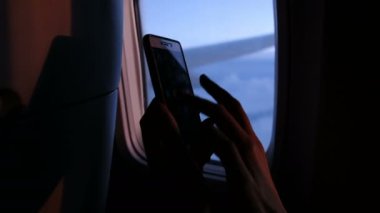 Pencere lombar arka plan ve uçak iin kanat gemide Smartphone kullanarak akşam. Parmak dokunmatik ekran ve akıllı telefon yakın çekim kullanın.