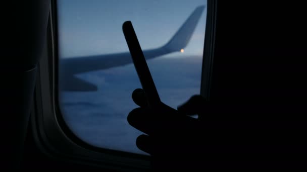 Per Smartphone und wählt eine Nachricht auf dem Handy im Flugzeug gegen das Fenster des Bullaugen während des Fluges am Abend. Finger berühren den Bildschirm aus nächster Nähe. — Stockvideo