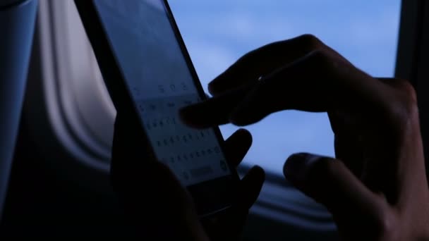 在傍晚的飞行中, 女人用手机在飞机上的窗户上拨出一条信息。手指触摸屏幕, 使用智能手机特写. — 图库视频影像