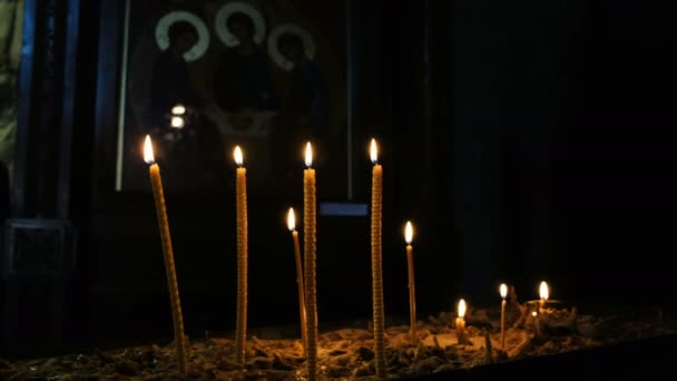 Wachskerzen brennen und stehen im Sand in der orthodoxen Kirche des antiken Tempels auf dem Hintergrund der Ikone der heiligen Dreifaltigkeit — Stockvideo