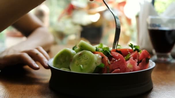Nő kezd eszik egy saláta, friss zöldségek uborka és paradicsom, lassú mozgás. A helyes táplálkozás, egészséges vegetáriánus ételek Premier plán fogalma.