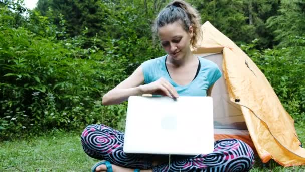 Kadın turist serbest meslek sahibi bir dizüstü bilgisayar bir kamp açar ve doğaya karşı bir turist çadır zemin çalışır. — Stok video