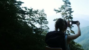 Genç kadın turist sırt çantası ile smartphone güzel panoramik manzaralı tepeler ve dağlar, kamera hareketi ile selfie alır