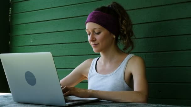 Улыбающаяся деловая женщина туристический фрилансер, печатающая на ноутбуке на открытом воздухе летом у зеленой стены — стоковое видео
