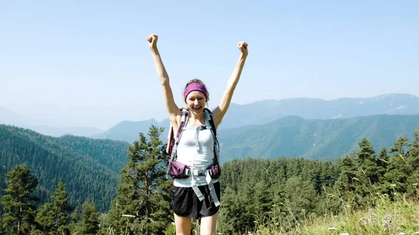 妇女旅游与背包举起她的手和跳跃从幸福的背景下一个美丽的山区景观在远足。成功、目标成就和胜利的概念. — 图库照片