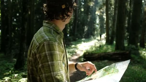 Touriste homme debout dans la forêt et vérifie l'itinéraire sur une carte papier et regarde le chemin — Video