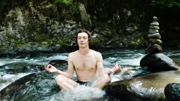 Ember meditál a lótusz helyzet, egy hideg hegyi folyó között a kövek és a cairn — Stock videók