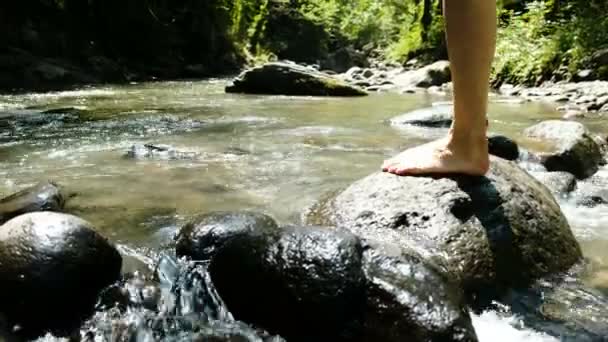 Молода жінка в купальнику сидить на камені і бризкає воду в гірській холодній річці — стокове відео