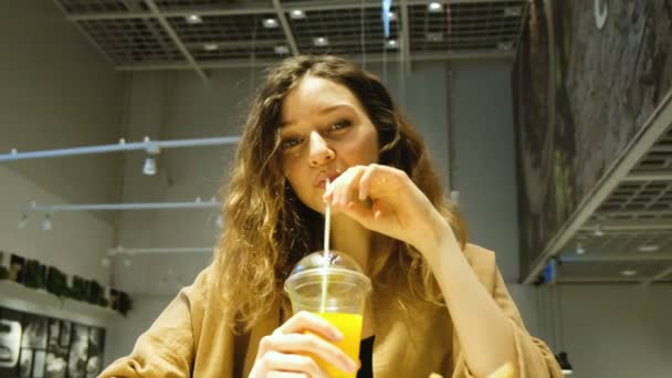 Молодая женщина пьет свежевыжатый сок в кафе — стоковое видео