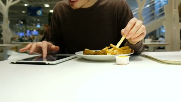 Человек быстро ест фаст-фуд и использует планшет в ресторане — стоковое видео