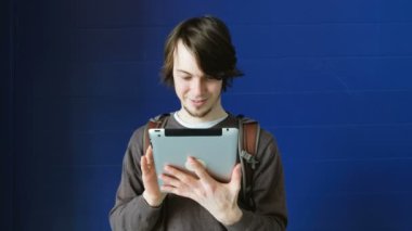 Öğrenci adam bir tablet bir mavi duvar arka plan üzerinde kullanır.