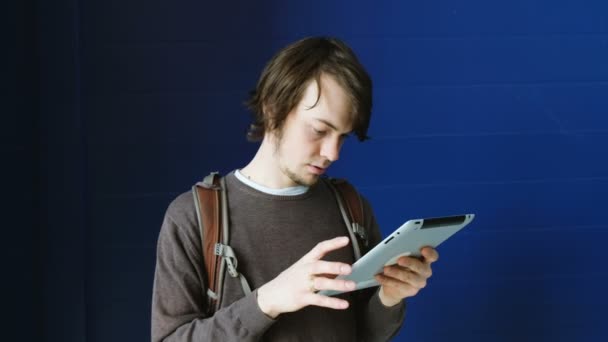 Joven hombre de negocios utiliza una tableta sobre un fondo de pared azul — Vídeos de Stock