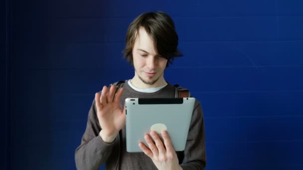 学生男がビデオ コミュニケーションと水色の壁の背景で友達とおしゃべりのタブレットを使ってください。 — ストック動画