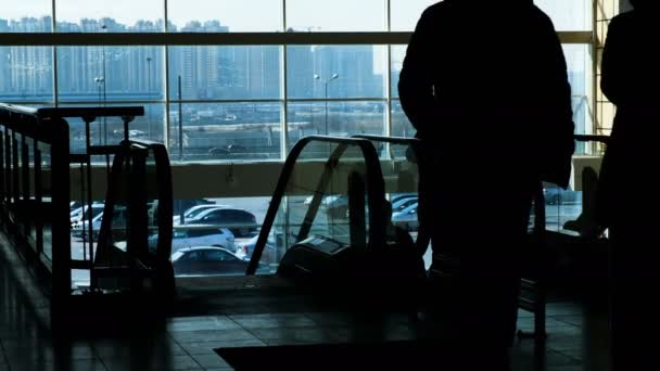 Silhouettes de personnes sur un escalier roulant dans un centre commercial en arrière-plan de gratte-ciel — Video