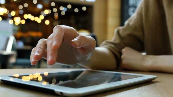 Mujer mano utiliza una PC tableta sobre un fondo borroso en la cafetería, primer plano — Vídeos de Stock