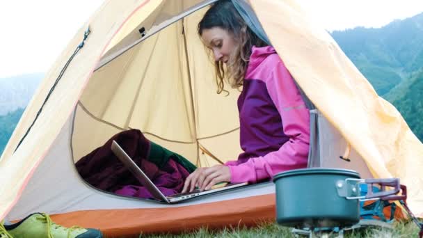 Boldog lány turisztikai használ egy laptop ülve, egy sátorban, szabadúszó nyomtatja ki, természet, utazás — Stock videók