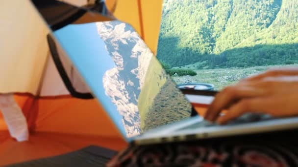 Las montañas se reflejan en la pantalla del ordenador portátil. Freelancer mujer utiliza el ordenador en tienda de campaña turística . — Vídeo de stock