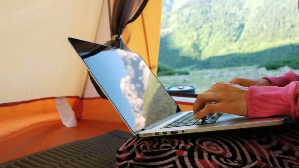 Las montañas se reflejan en la pantalla del ordenador portátil. Mujer freelancer utiliza el ordenador en una tienda de campaña turística, escribiendo en el teclado — Vídeo de stock