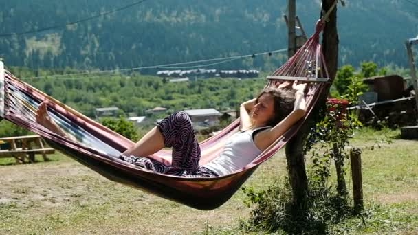 Dívka spí v houpací síti na povaze na pozadí zelených hor, pomalý pohyb — Stock video