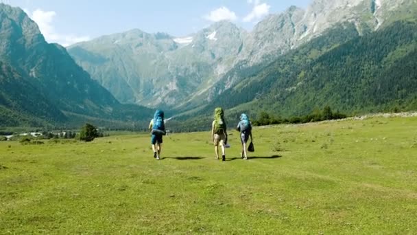 Turistas excursionistas con grandes mochilas están caminando en las montañas en una caminata contra el telón de fondo de un hermoso paisaje . — Vídeos de Stock