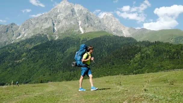 Unavený turista s velkým batohem padá k zemi na výlet na pozadí krásné horské krajiny. — Stock video