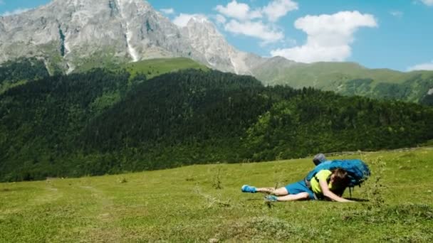 Um turista cansado com uma grande mochila se levanta do chão em uma caminhada contra o pano de fundo de uma bela paisagem montanhosa, um homem doente lentamente se levanta e caminha — Vídeo de Stock