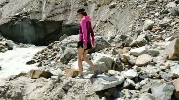 Chica turista va por las rocas a un río de montaña — Vídeos de Stock